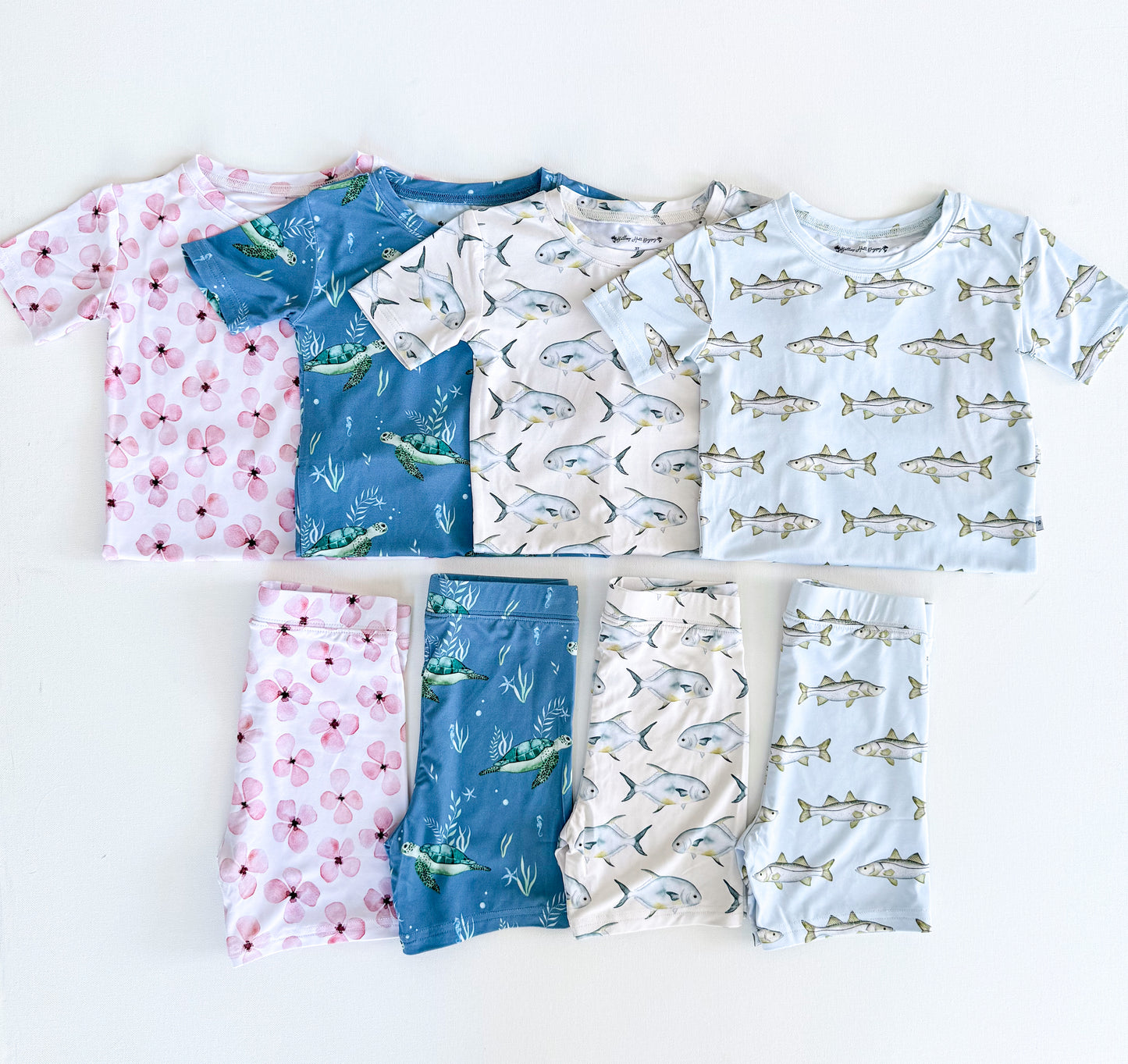 Set of children's short sleeve pajamas with floral, fish, and sea turtle patterns on a white background