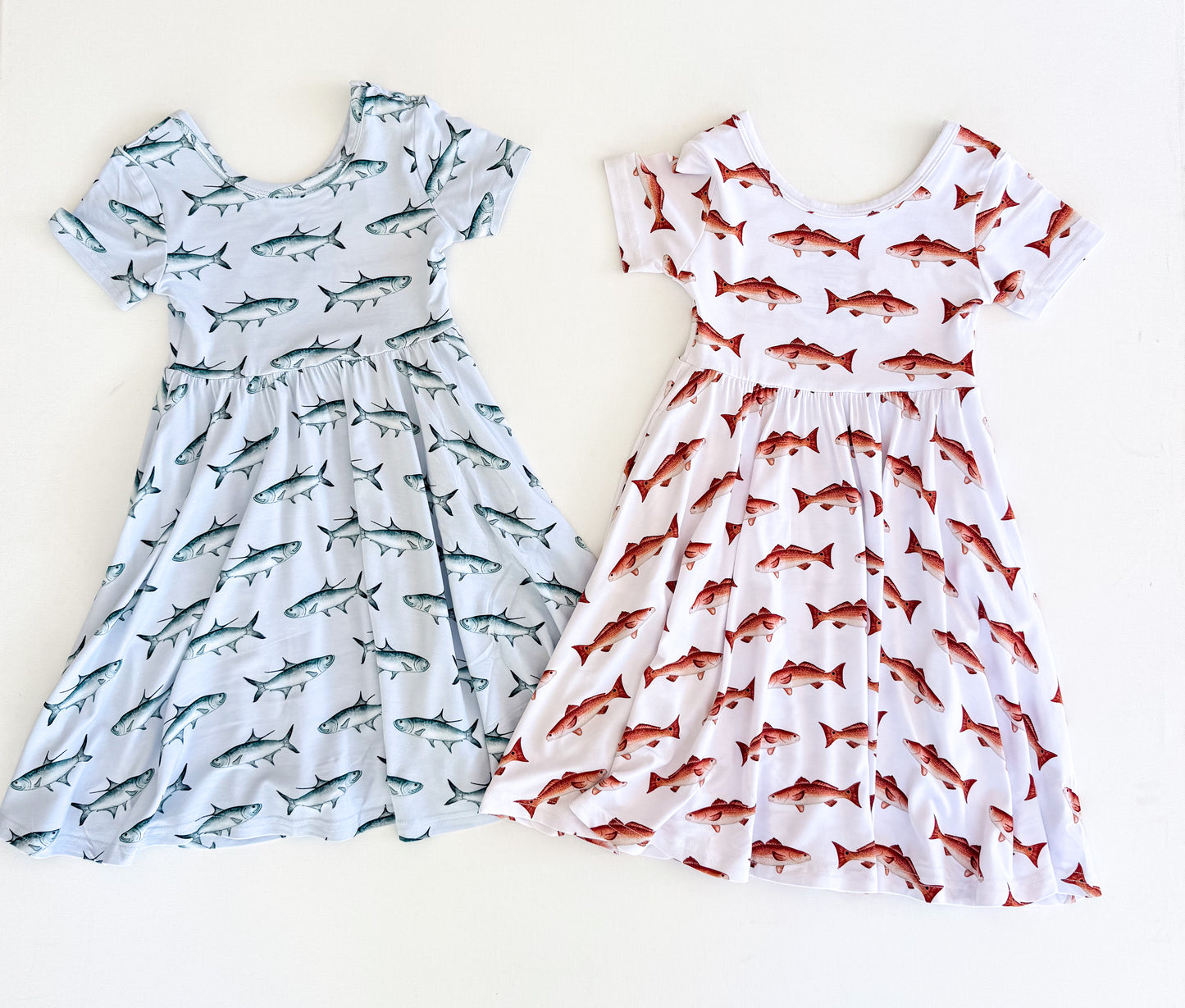 Flatly picture of two short sleeved twirl dresses, one with a blue background and blue tarpon, the other with a white background and redfish