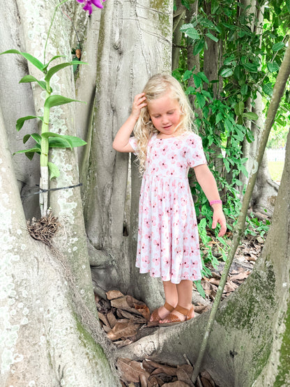 Customer provided photo of a little girl next to a tree wearing a short sleeve twirl dress with white background and pink flowers