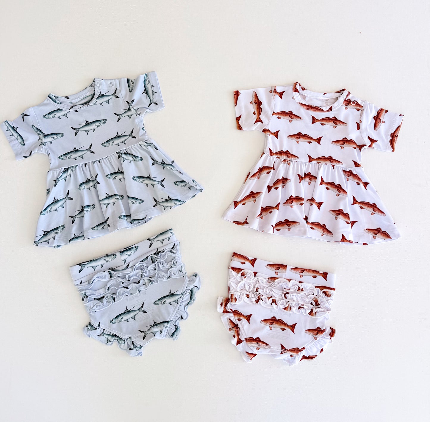 Flat lay of two peplum and ruffle bloomer sets one with light blue background with Tarpon one with white background with red fish both have a snap on the left shoulder and short sleeves