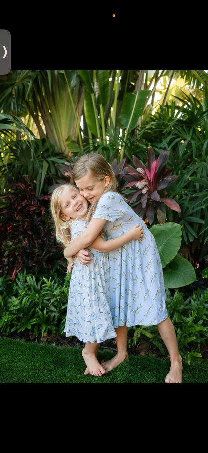 Two siblings hugging in short sleeved, twirl dresses, one with a yellow background and a permit fish, the other with a light blue background and snook fish
