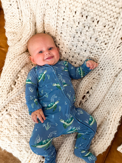 Baby wearing a blue sea turtle zippy onesie lying on a textured blanket