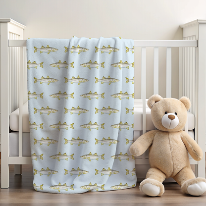 Crib with a light blue snook blanket featuring fish patterns and a teddy bear.