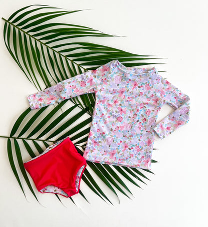 Floral long-sleeve shirt and hot pink swim bottoms on a palm leaf