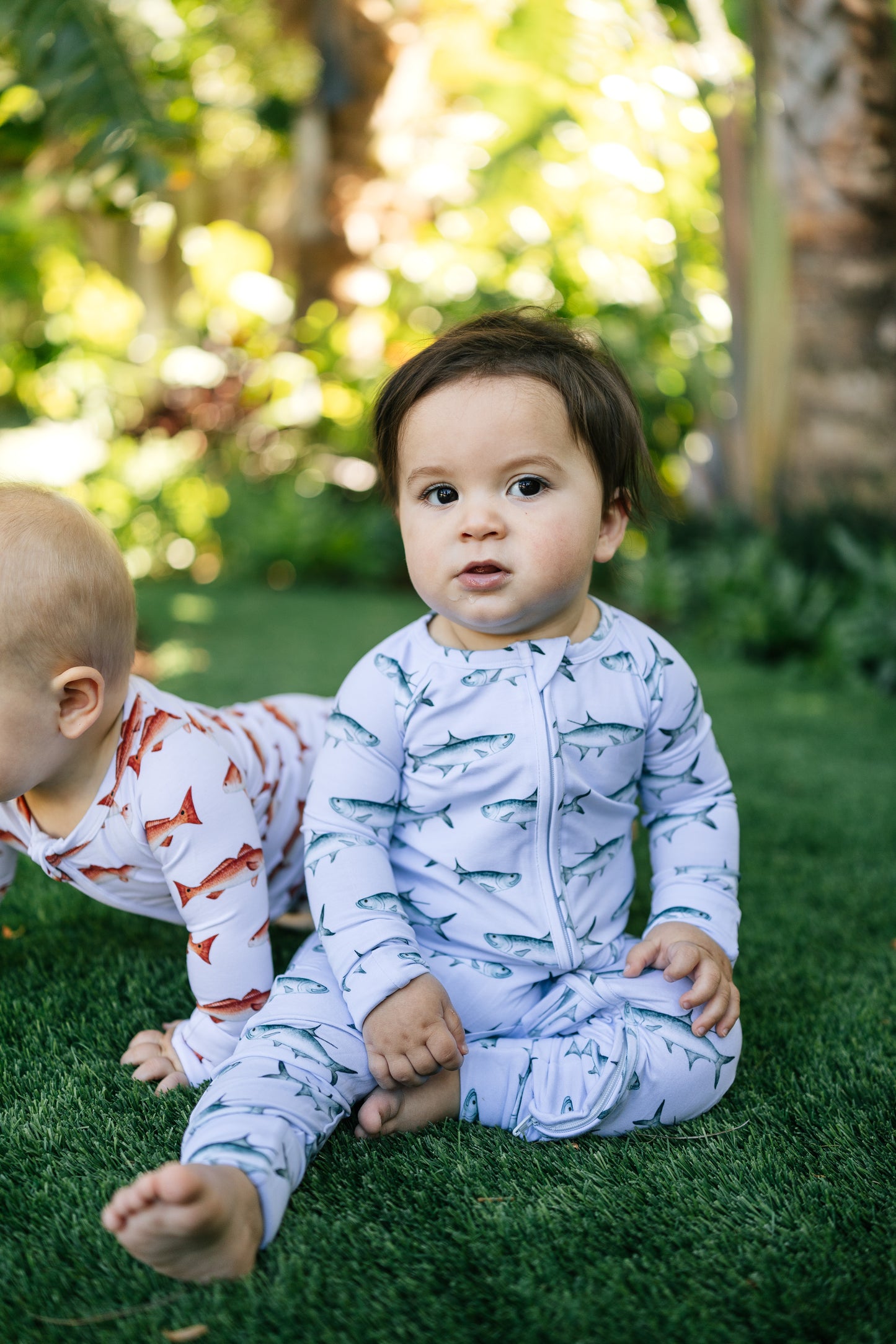 Two children in tarpon and redfish pajamas standing on grass with a blurred natural background
