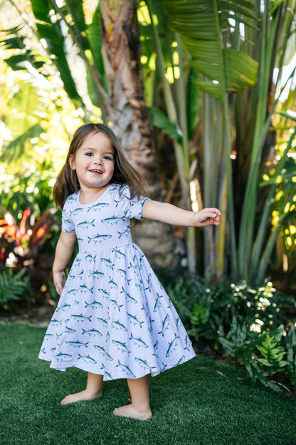Little girl twirling in Tarpon dress with light blue background and tropical foliage