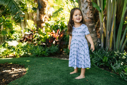 Little girl twirling in Tarpon dress with light blue background and tropical foliage