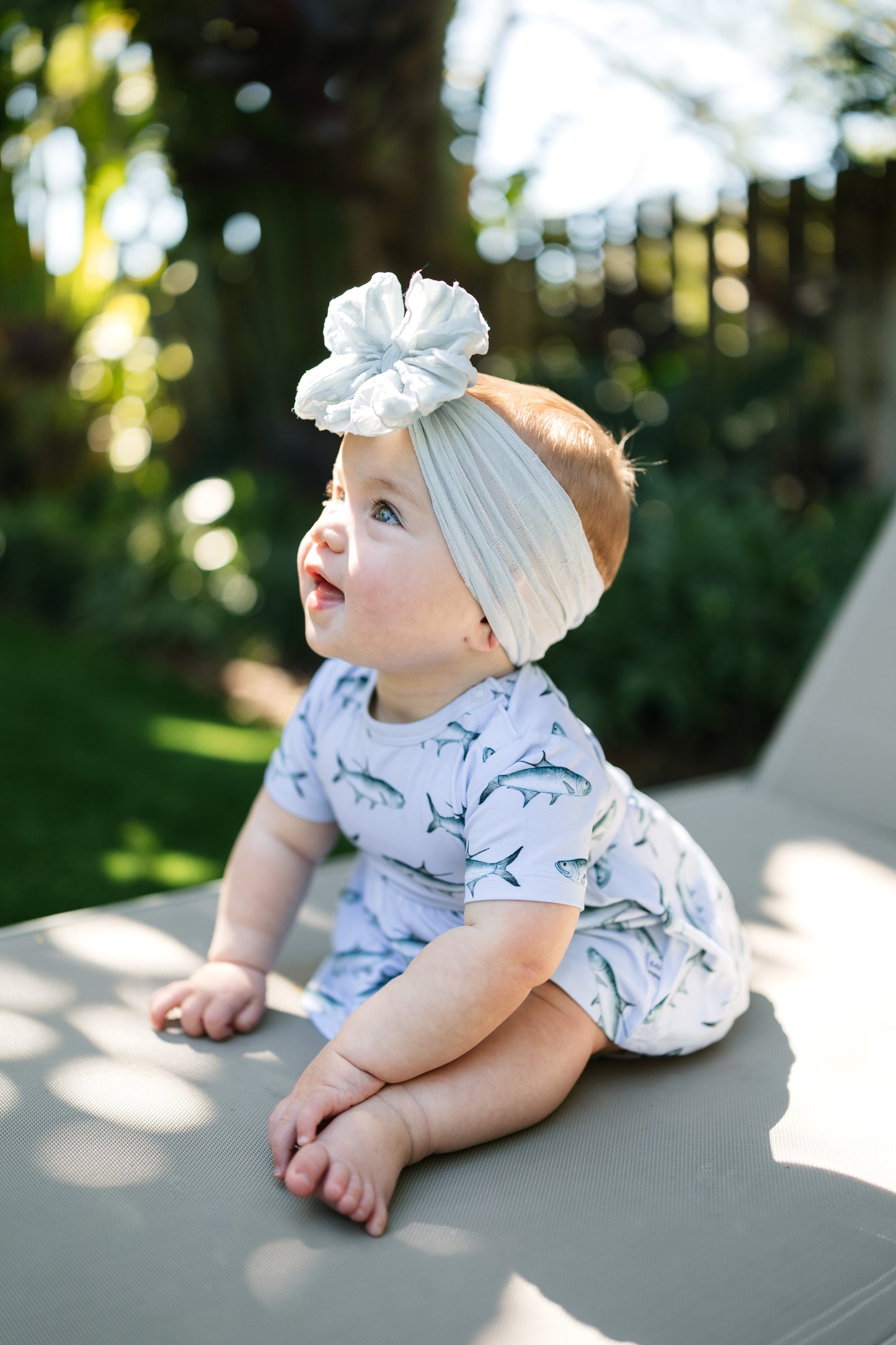 baby sitting on a lawn chair wearing Tarpon peplum and bloomer set with a big white bow.