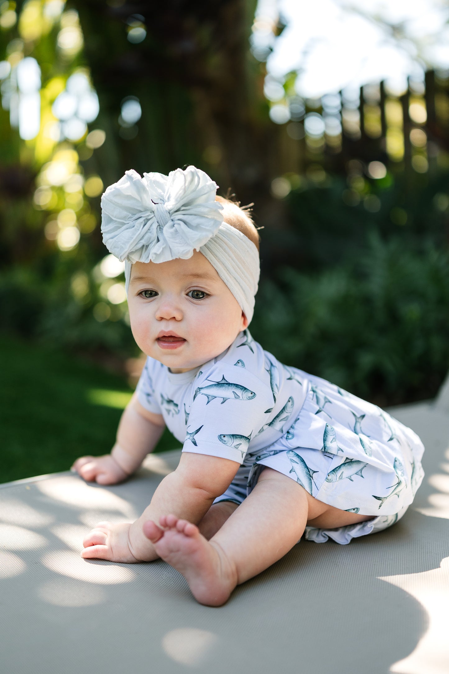 baby sitting on a lawn chair wearing Tarpon peplum and bloomer set with a big white bow.