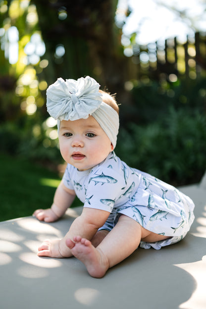 baby sitting on a lawn chair wearing Tarpon peplum and bloomer set with a big white bow.
