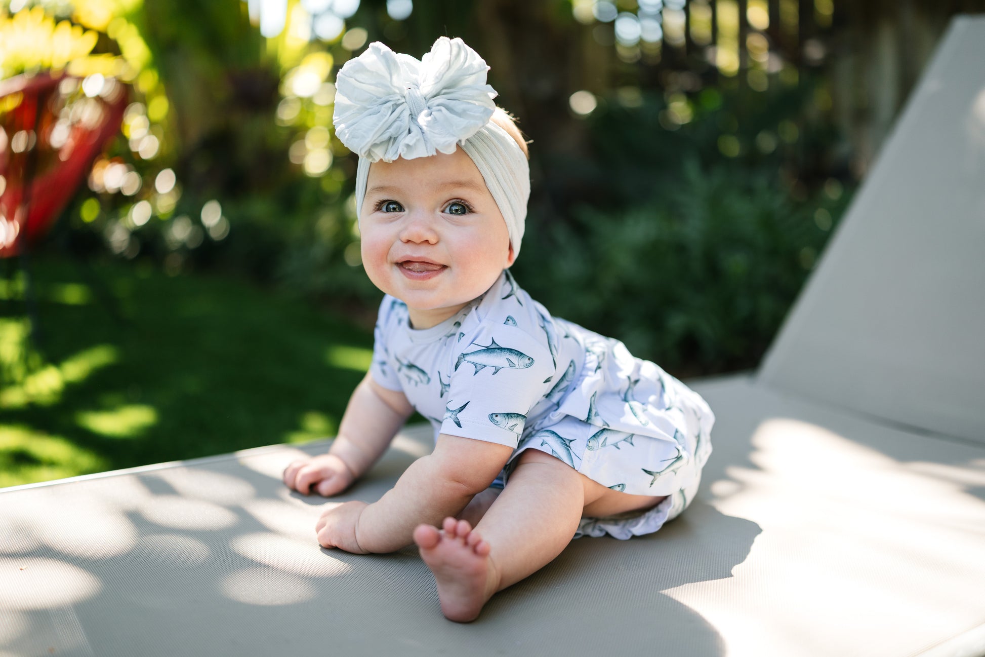 baby sitting on a lawn chair wearing Tarpon peplum and bloomer set with a big white bow.