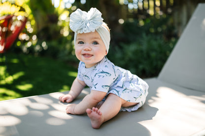 baby sitting on a lawn chair wearing Tarpon peplum and bloomer set with a big white bow.