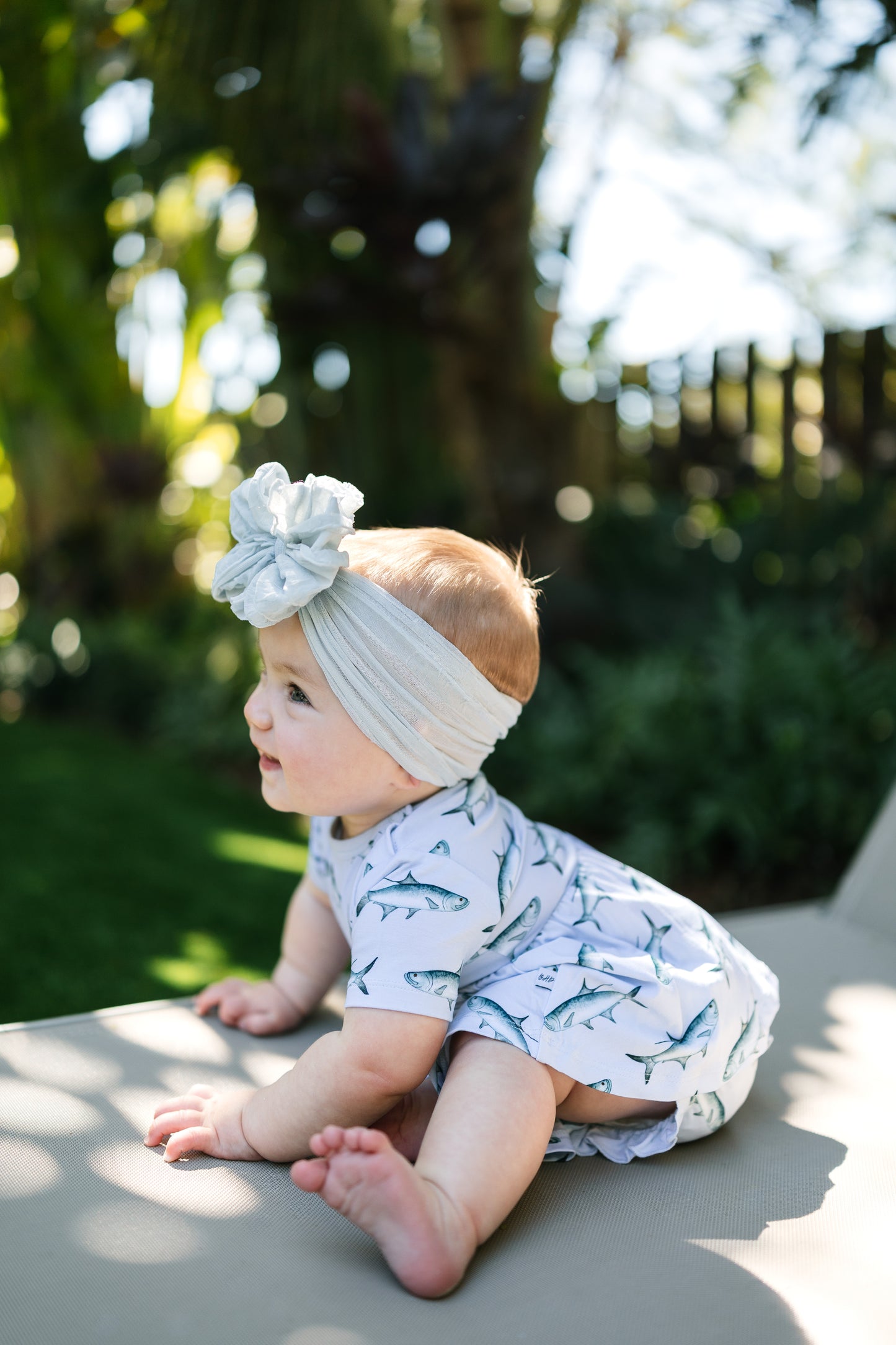 baby sitting on a lawn chair wearing Tarpon peplum and bloomer set with a big white bow.