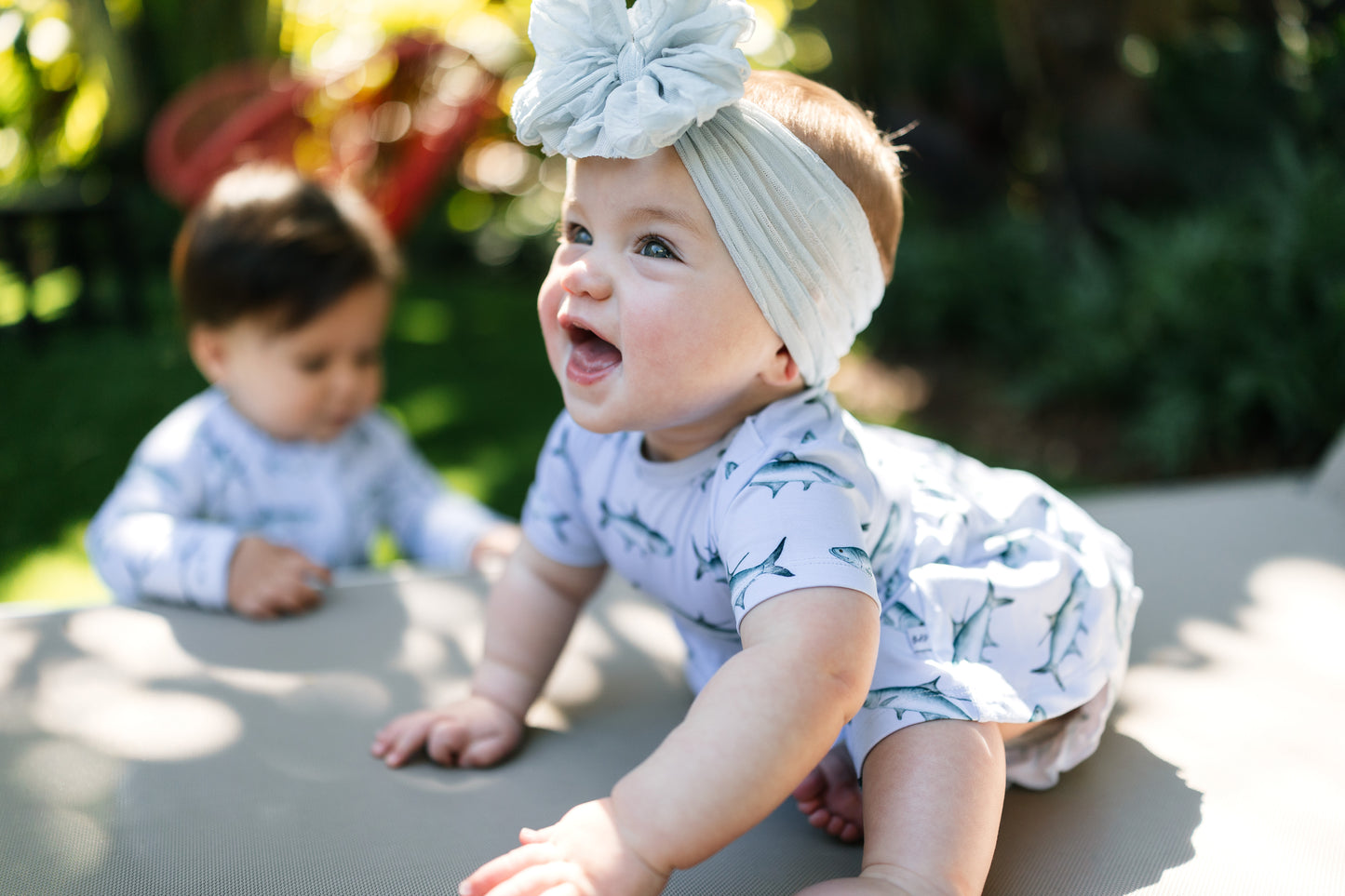 Two babies in matching Tarpon outfits outdoors on a sunny day.