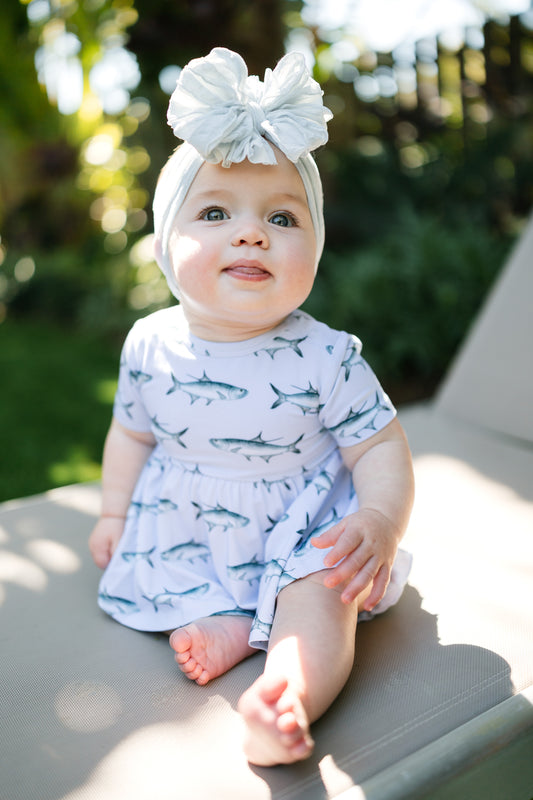 baby sitting on a lawn chair wearing Tarpon peplum and bloomer set with a big white bow.