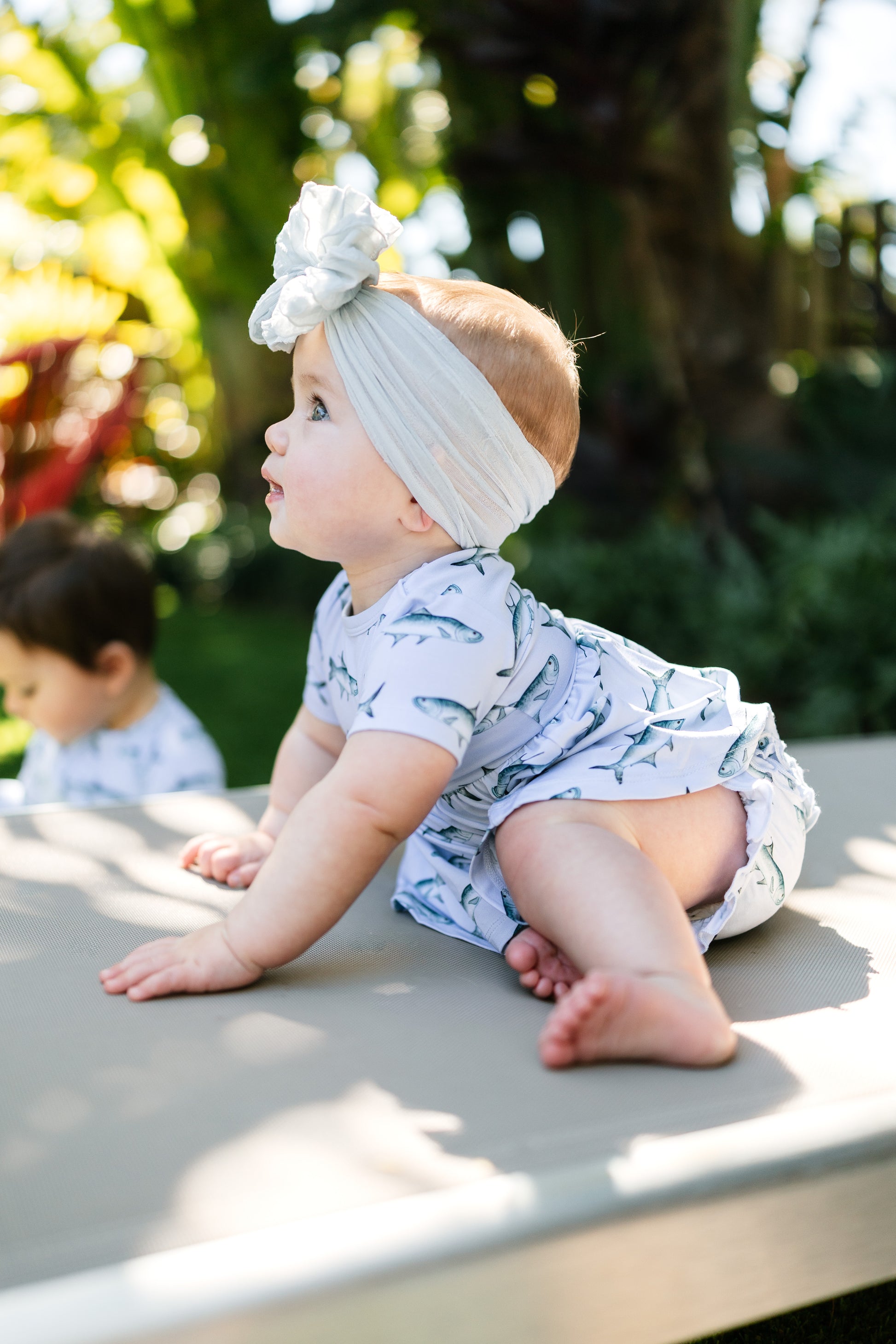 baby sitting on a lawn chair wearing Tarpon peplum and bloomer set with a big white bow.