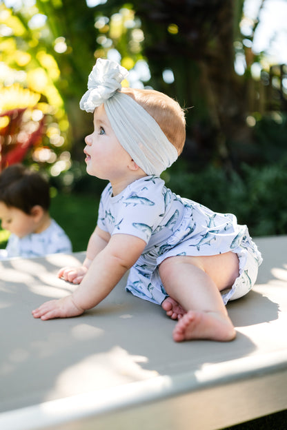 baby sitting on a lawn chair wearing Tarpon peplum and bloomer set with a big white bow.