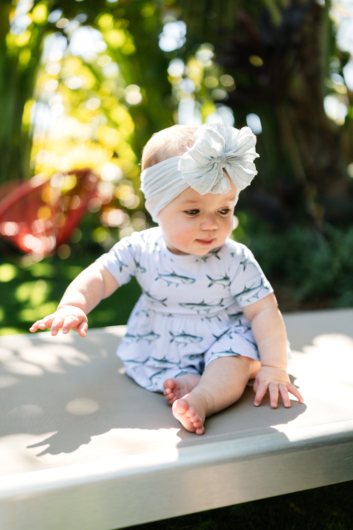 baby sitting on a lawn chair wearing Tarpon peplum and bloomer set with a big white bow.