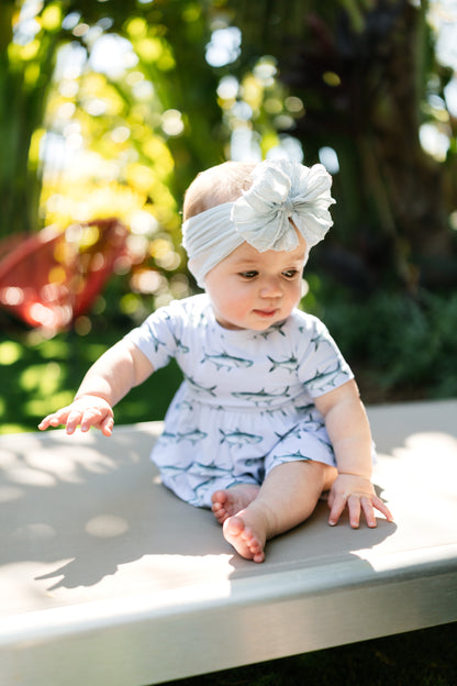 baby sitting on a lawn chair wearing Tarpon peplum and bloomer set with a big white bow.