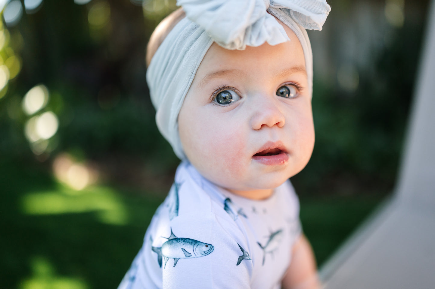 closeup of baby wearing tarpon peplum and a big white bow with big blue eyes