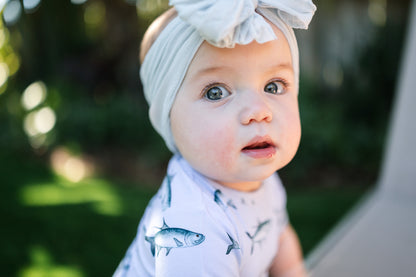 closeup of baby wearing tarpon peplum and a big white bow with big blue eyes