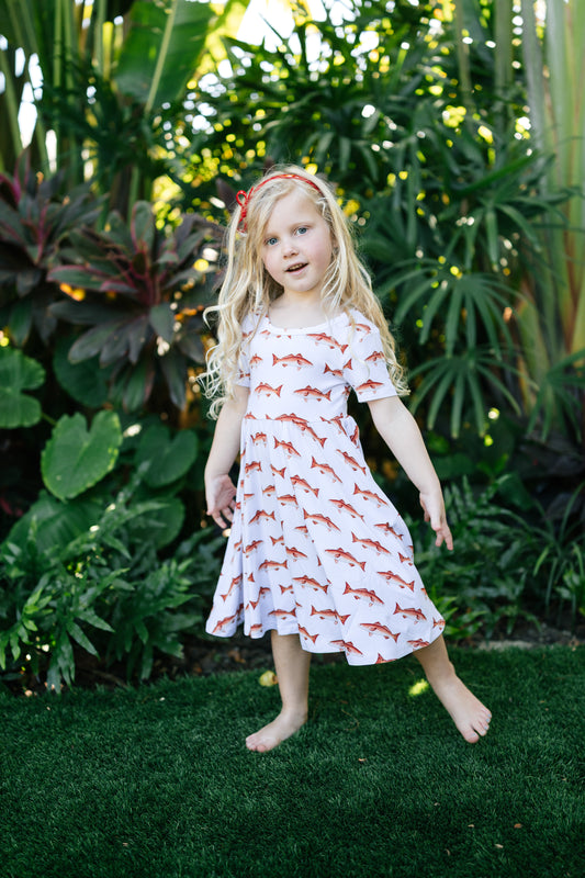 Little girl wearing a redfish seaside dress with a white background outdoors