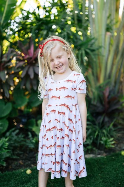 Little girl wearing a redfish seaside dress with a white background outdoors