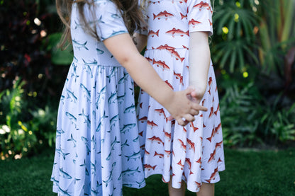 Two children holding hands wearing dresses with fish patterns in a garden setting.