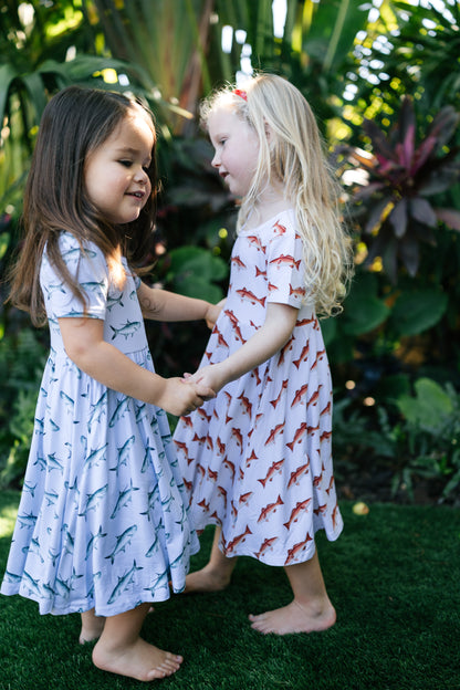 Two children in patterned dresses standing outdoors with greenery in the background