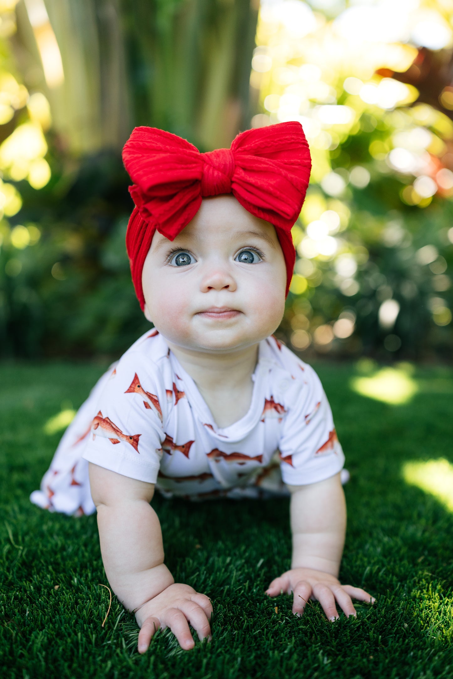 baby in redfishcrawling smiling outdoors with a big red bow