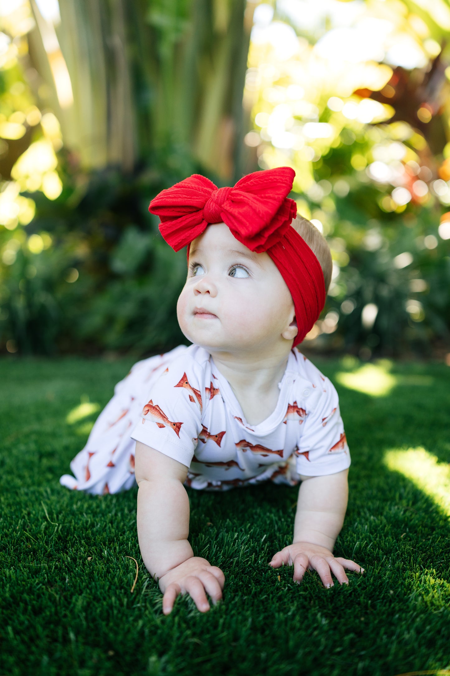 baby in redfish pattern crawling outdoors with a big red bow