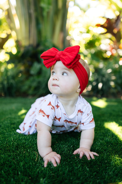 baby in redfish pattern crawling outdoors with a big red bow