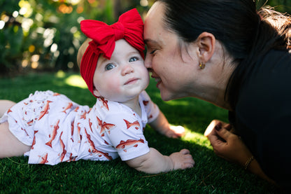 Baby wearing a red bow lying on grass snuggling her mom