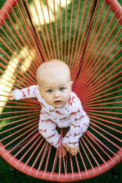 Baby lying on a red woven chair with a blurred green background wearing a redfish zippy