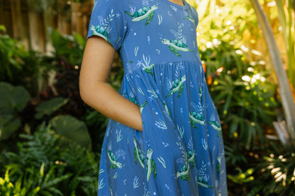 Close-up of the short sleeve twirl dress with blue background and sea turtles with hands in the pockets