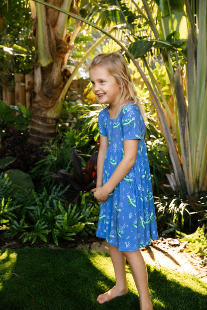 Young girl in a blue sea turtle seaside dress standing in a garden with greenery around