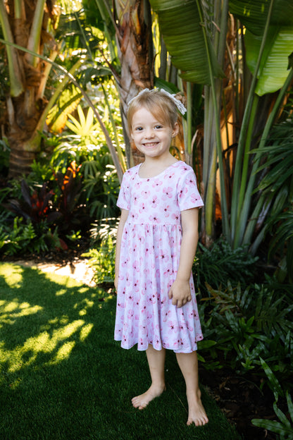 Little girl posing with a tropical background, wearing a white twirl dress with short sleeves and pockets