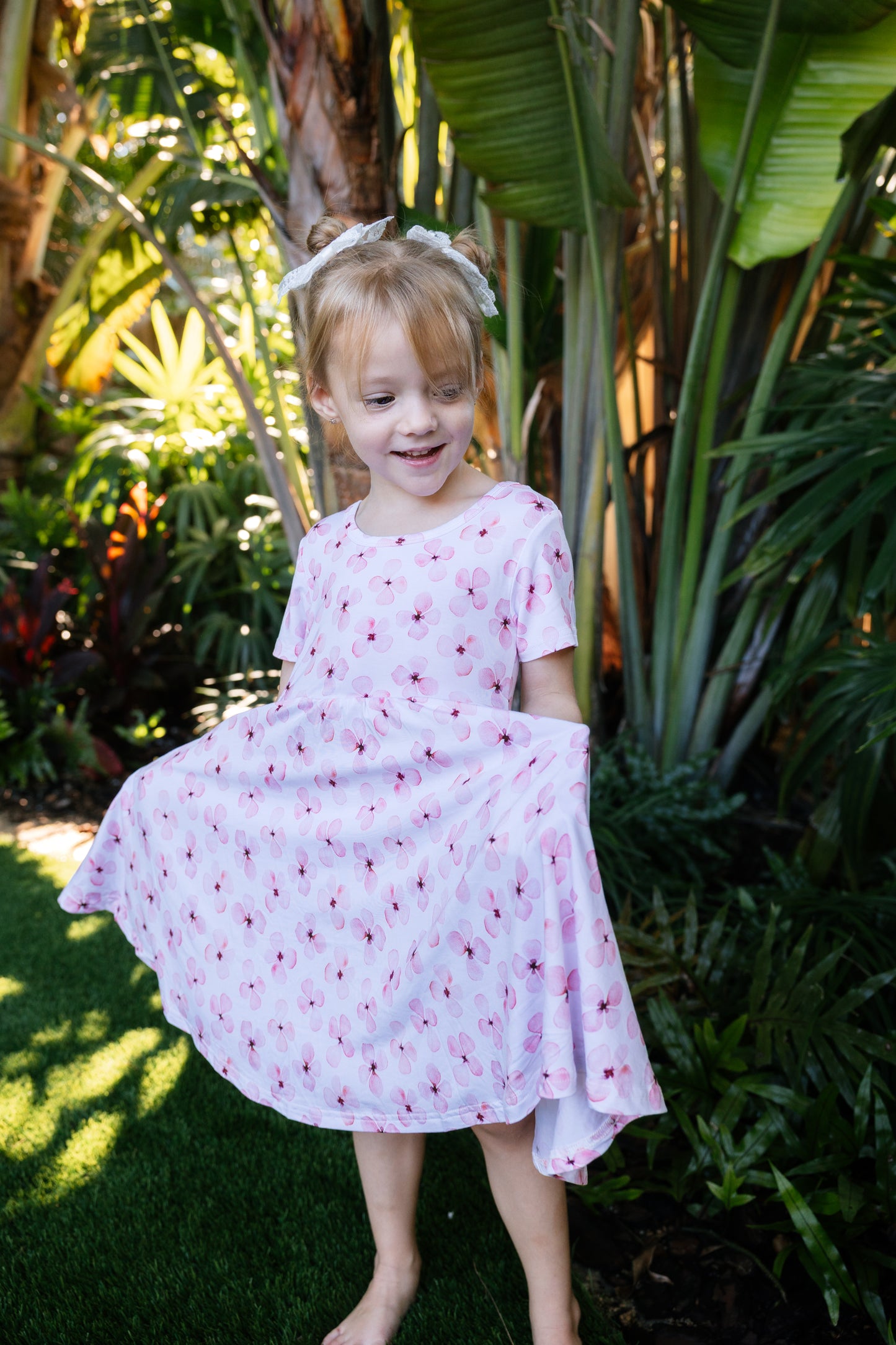 Little girl posing with a tropical background, wearing a white twirl dress with pink flowers short sleeves and pockets