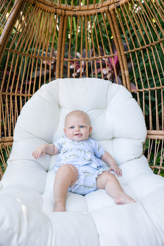 And sitting in a bamboo chair with a white cushion, wearing the light blue ruffle, plum, and bloomer set with snook on it