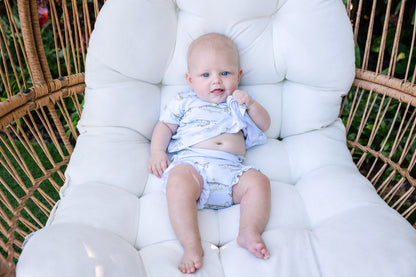 Baby sitting on a white cushioned chair outdoors wearing light blue snook peplum and ruffle bloomers set