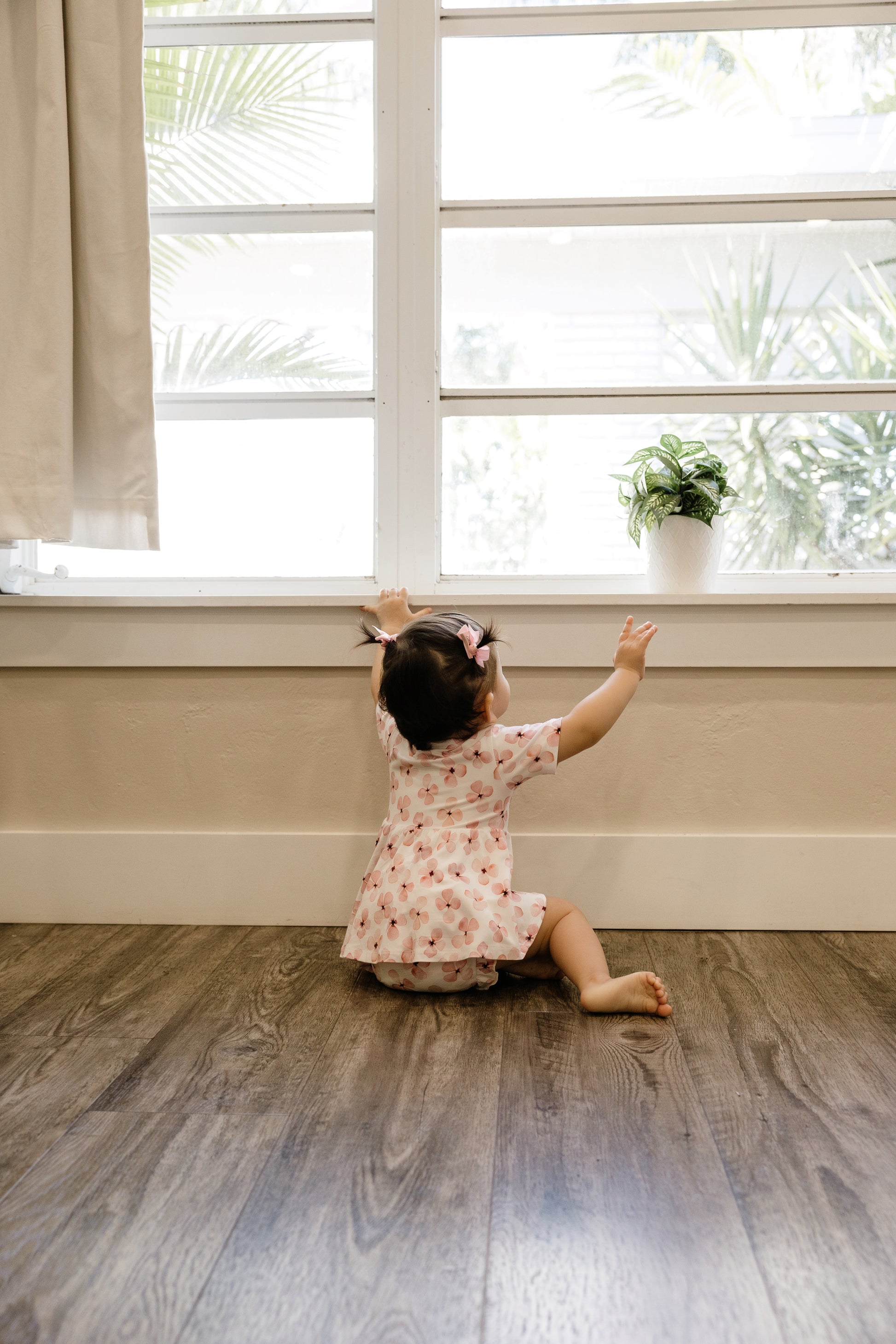Baby wearing pink floral peplum and bloomers looking out window