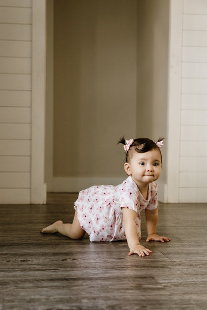Infant crawling on the ground, wearing the white ruffle, plum and bloomer set with pink flowers