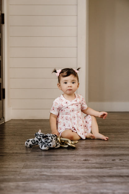 Toddler sitting on the floor, wearing the peplum and ruffle bloomer set white background with pink flowers