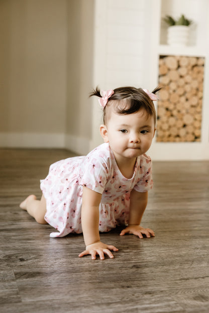 Child in a white peplum with pink flowers crawling on a wooden floor