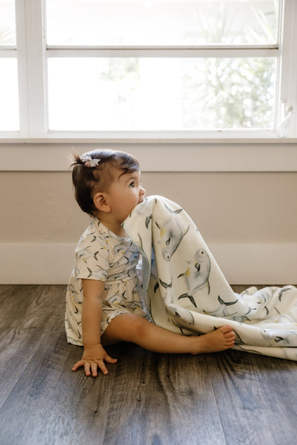 Child sitting on a wooden floor with a blanket, looking out a window wearing yellow peplum and ruffle bloomers set with permit on it