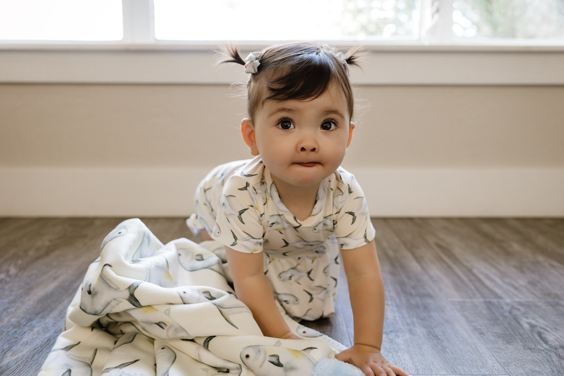Baby in Permit ruffle bloomer peplum set sitting on a wooden floor with a Permit blanket