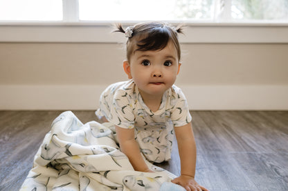 Baby in Permit ruffle bloomer peplum set sitting on a wooden floor with a Permit blanket
