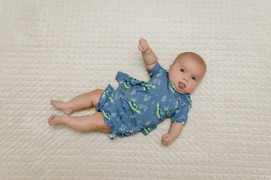 baby laying on a bed wearing blue peplum and ruffle bloomers set with sea turtles on it