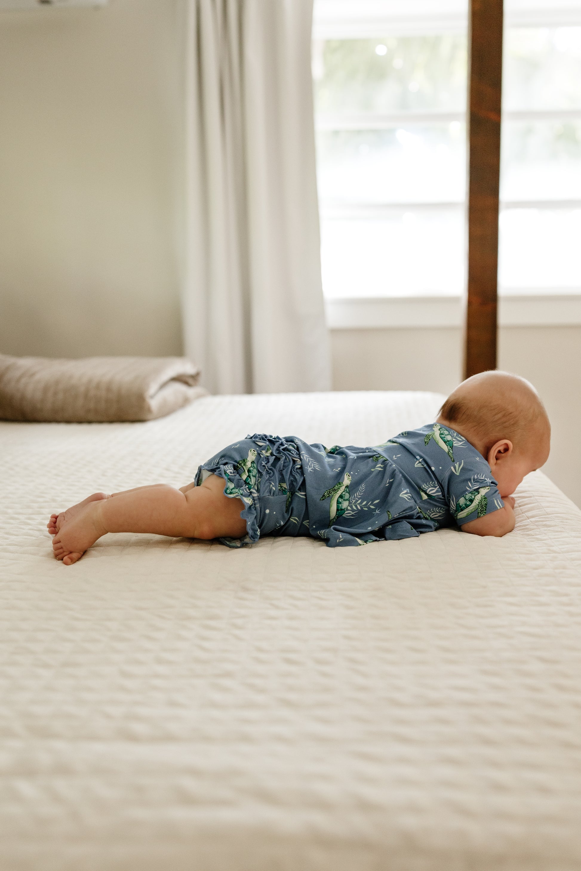 Baby laying on bed in sea turtle peplum and ruffle bloomers set.