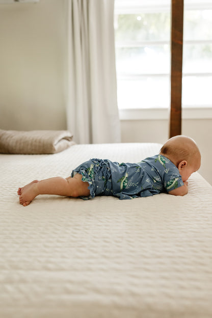 Baby laying on bed in sea turtle peplum and ruffle bloomers set.